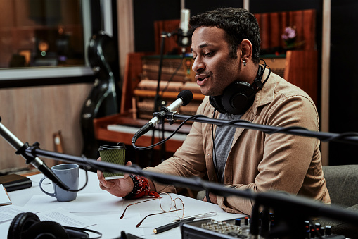 Retrato del joven presentador de radio masculino tomando una copa, mirando enfocado mientras habla en el micrófono, moderando un show en vivo photo