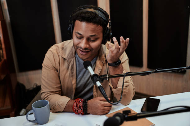 Happy young male radio host talking, broadcasting in studio using microphone and headphones Happy young male radio host talking, broadcasting in studio using microphone and headphones. Communication and entertainment concept. Selective focus. Horizontal shot radio dj stock pictures, royalty-free photos & images