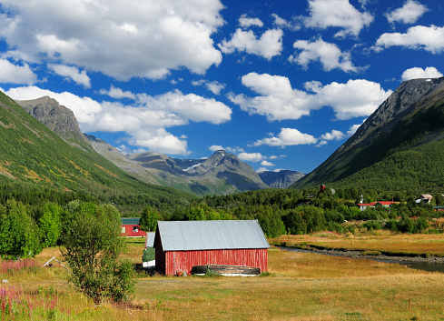 Red Wooden Barn Surrounded By Mountains Near Olderdalen On A Sunny Summer Day With A Clear Blue Sky And A Few Fluffy Clouds