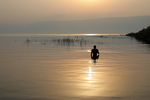 Man silhouette enters to Galilee Lake in Israel at sunrise.