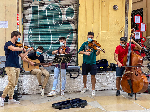 Valencia, Spain - October 9, 2020: Group of young men playing chord instruments in the historic town of the city. Music students sometimes play in the street not only to receive tips for their performance but also to have a chance to practice