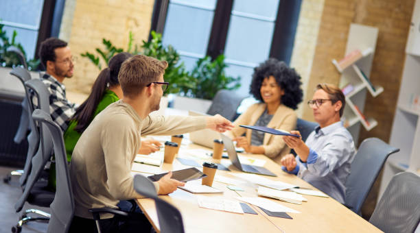 istock Caucasian man giving a folder with documents to his young colleague while having a meeting with project team in the modern office 1279609664