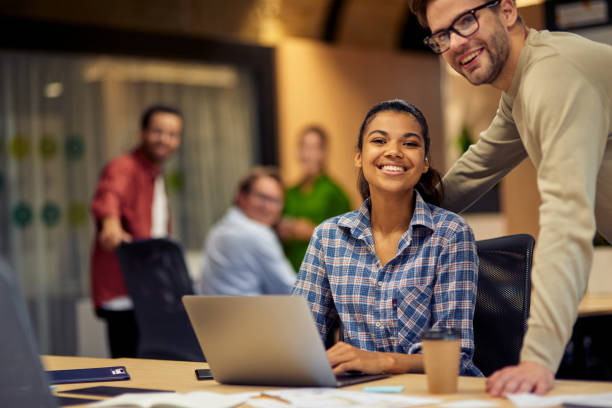 istock Two young multiracial colleagues looking at camera and smiling while working together on laptop in the modern office or coworking space 1279609757