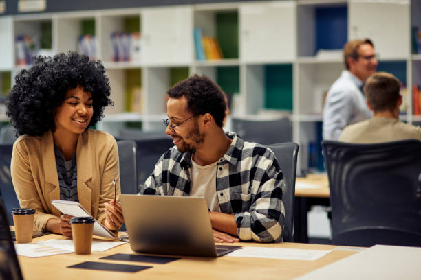 istock Two young diverse business colleagues discussing project, sharing fresh ideas while sitting at the desk and working together in coworking space 1279609759