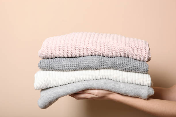 istock A stack of sweaters in female hands on a colored background. Warm clothes. 1279611437