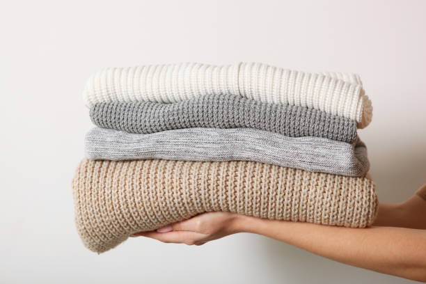 istock A stack of sweaters in female hands on a colored background. Warm clothes. 1279612348