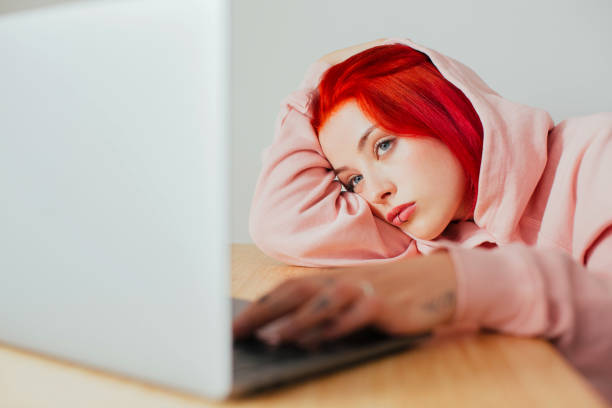 retrato de una joven aburrida acostada en el escritorio usando en el ordenador portátil para navegar por internet - exceso fotos fotografías e imágenes de stock