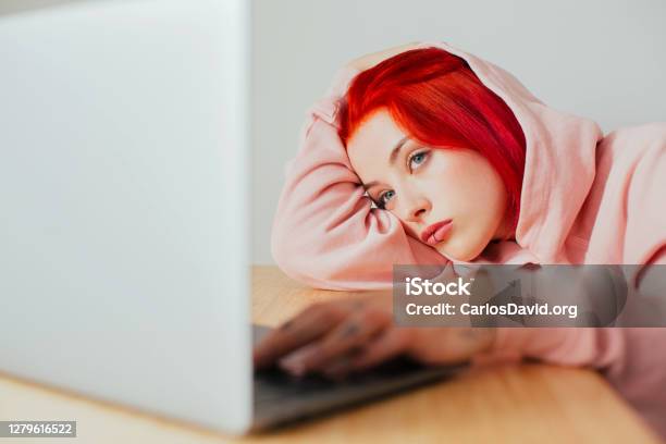 Portrait Of A Young Woman Bored Lying On Desk Using In Laptop Computer To Surf Internet Stock Photo - Download Image Now
