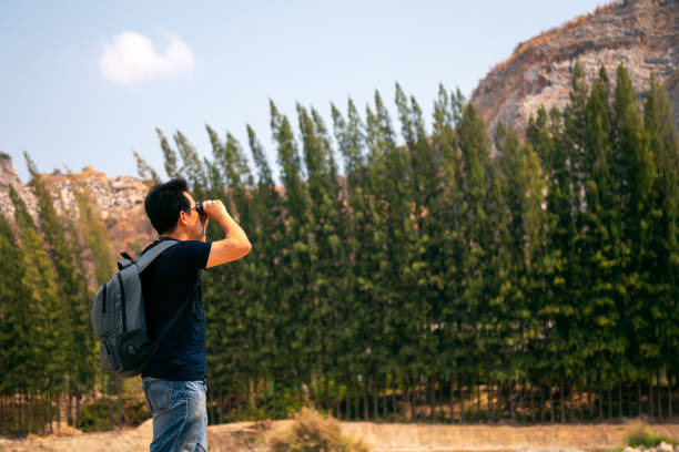 Young Asian tourist trekking with backpack holding binoculars for seeing mountain peak