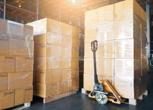 istock Cargo boxes shipment, Manufacturing and warehousing. Stack of cardboard boxes on pallet and hand pallet truck at the warehouse storage. 1279624449