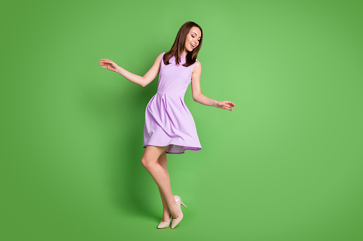 Full size photo adorable sweet careless girl lady look down hands side prom party, dress air blow slim legs shoe shop advert concept wear purple dress isolated pastel green color background