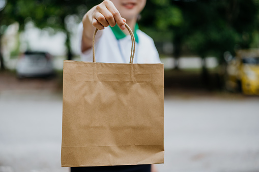 Young Asian delivery woman delivering goods in paper bag to customer