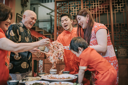 asian chinese family with traditional clothing celebrating chinese new year reunion dinner having traditional dishes raw fish lau sang symbolize prosperity, wealth and health