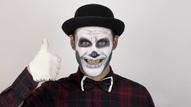 A horrible man in clown makeup smiles and shows a thumb up. A scary clown looks at the camera and laughs terribly. Scary grimaces of a clown looking at the camera A horrible man in clown makeup smiles and shows a thumb up. A scary clown looks at the camera and laughs terribly. Scary grimaces of a clown looking at the camera. Halloween costume. evil joker silhouette stock pictures, royalty-free photos & images