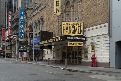 Manhattan, New York. June 02, 2020. A man wearing a red uniform walks past the Broadway Golden Theatre on west 45th street in Midtown.  Broadway performances were suspended on March 12, 2020 when 31 productions were running, including 8 new shows in previews.