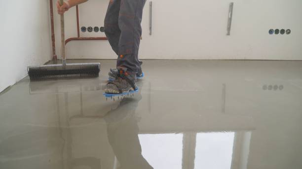 a worker rolls out the liquid floor with a trowel. squeegee for distributing the mixture. the worker levels the liquid floor. finishing works - needle roller for bulk floor - levelling instrument imagens e fotografias de stock