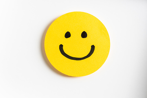 Drawing of a happy smiling emoticon on a yellow paper and white background. Hapiness concept.