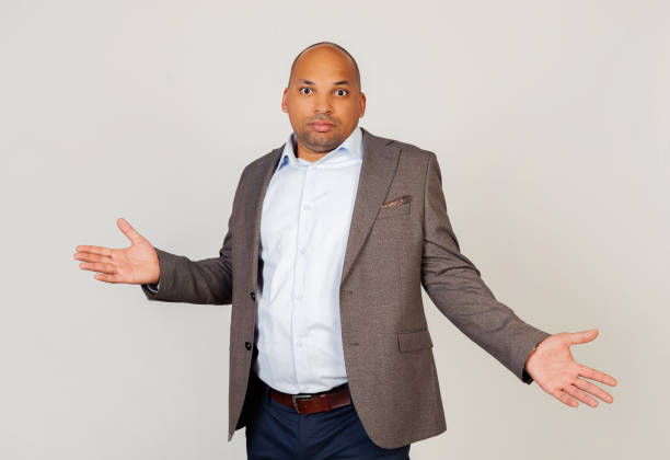 young male african american businessman looking at the camera, spread his hands guiltily. an ignorant and confused expression with raised arms and hands. doubt concept. - blank expression head and shoulders horizontal studio shot imagens e fotografias de stock