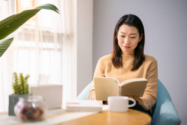 istock Young woman reading a book at home 1279645339