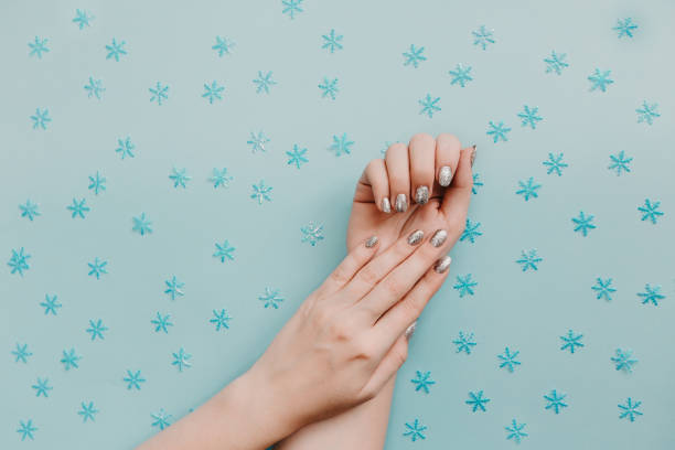 Female hands with silver manicure on blue background with snowflakes. Female hands with silver manicure on blue background with snowflakes. Holiday, New Year, shiny sparkles. christmas nails stock pictures, royalty-free photos & images