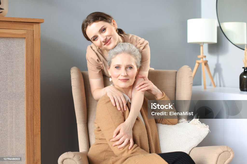 Elderly middle mother sitting in a chair and her daughter are hugging, looking at camera, trusted relations. Elderly middle mother sitting in a chair and her daughter are hugging, looking at camera, trusted relations Adult Stock Photo
