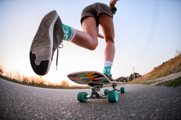 vista ad angolo basso della ragazza che sta cavalcando lo skateboard sull'asfalto. - skateboard park foto e immagini stock