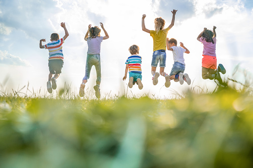 Happy children with arms raised are jumping in nature. Rear view