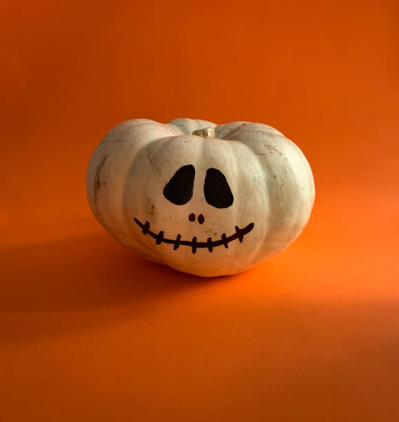 istock White Halloween pumpkin with spooky face on orange background 1279651613