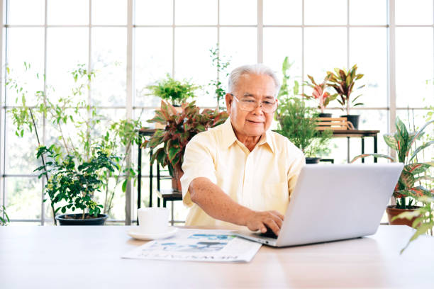 istock A senior retired old man dressed in casual style is using a laptop and smiling while sitting at home with indoor garden in the background. Retirement hobby and lifestyle. Grandfather work from home. 1279654083