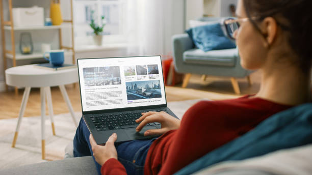 istock Young Woman at Home Is Using Laptop Computer for Scrolling and Reading News about Technological Breakthroughs. She's Sitting On a Couch in His Cozy Living Room. Over the Shoulder Shot 1279660342
