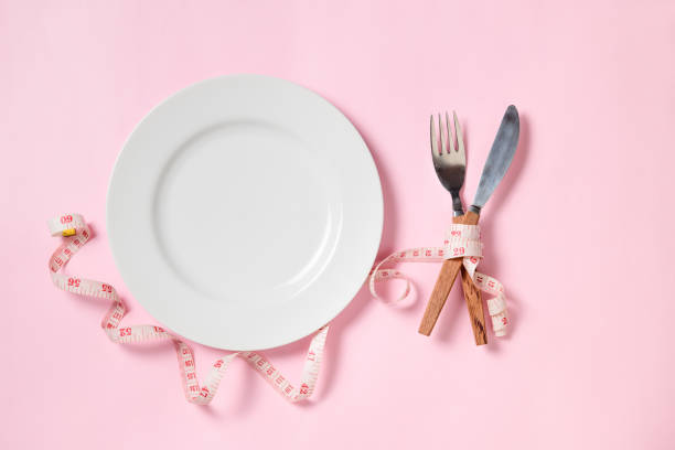 istock Empty white plate with a knife and fork wrapped in measuring tape on pink background. 1279660841
