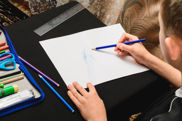 istock A boy sits at a table and draws pencils on white paper. 1279664215