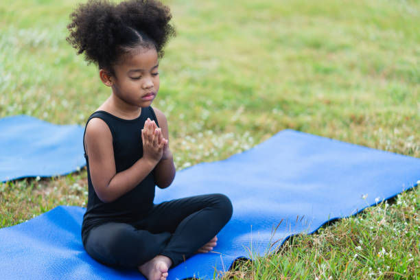 African american little girl sitting on the roll mat practicing meditate yoga in the park outdoor African american little girl sitting on the roll mat practicing meditate yoga in the park outdoor mindfulness children stock pictures, royalty-free photos & images