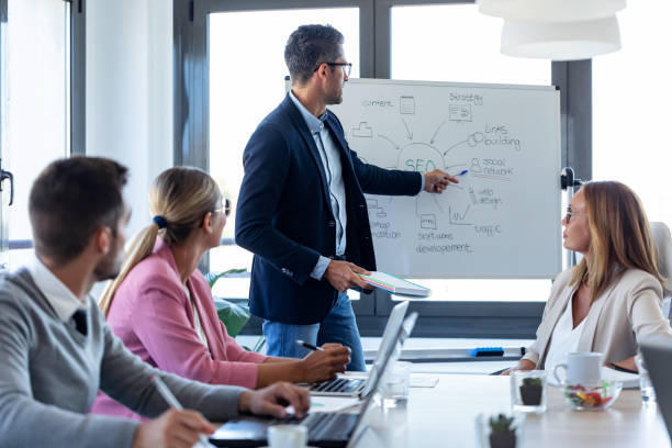istock Handsome businessman pointing at white blackboard and explain a project to her colleagues on coworking place. 1279670979