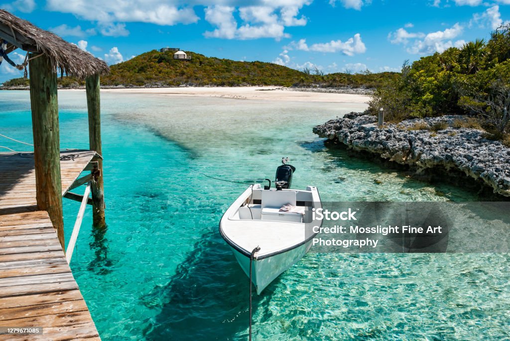 Small boat moored off a pier over turquoise ocean waters near private remote Exuma Islands in the Bahamas A small outboard motor boat moored to a wooden pier in the tropical paradise of the Exuma Islands of the Bahamas. Bahamas Stock Photo