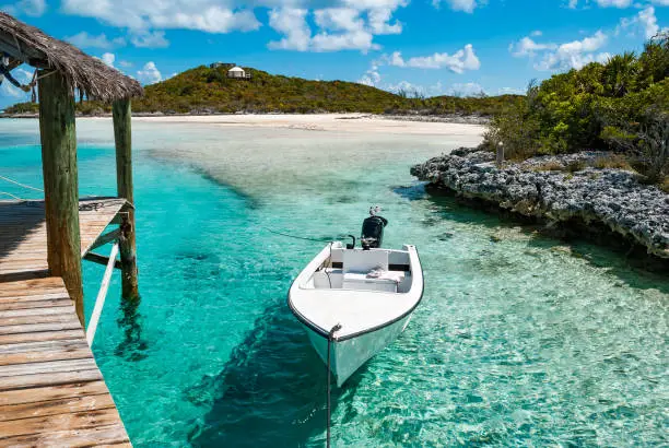 A small outboard motor boat moored to a wooden pier in the tropical paradise of the Exuma Islands of the Bahamas.