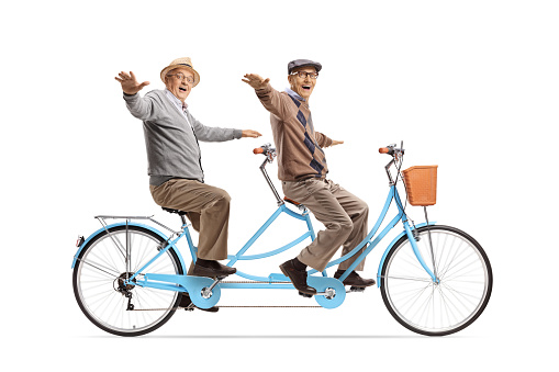 Cheerful elderly men riding a tandem bicycle and spreading arms isolated on white background