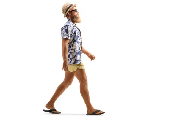 Full length profile shot of a bearded male tourist with sunglasses walking isolated on white background
