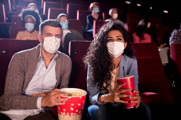 Happy couple wearing face masks at the cinema Couple wearing protective face masks while watching the movie at the cinema. film festival photos stock pictures, royalty-free photos & images