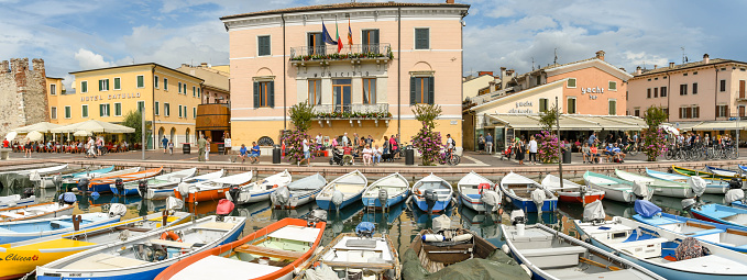 Bardolino, Lake Garda, Italy - September 2018:  Panoramic view of small fishing boats lined up in the small harbour in Bardolino on Lake Garda. In the centre is the town hall building.
