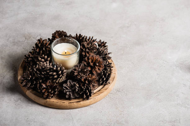 istock Scented candle with pine cones on wooden plate on grey and textured background 1279690299