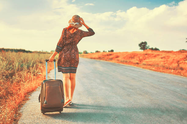 Young woman hitchhiking on the empty road on a sunny summer day.