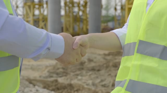 Businessman and business woman shaking hands as sign of cooperation at construction site