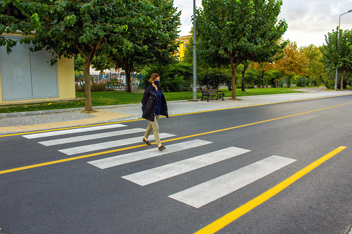 Young woman wearing protective mask and crossing street at crossway during the pandemic