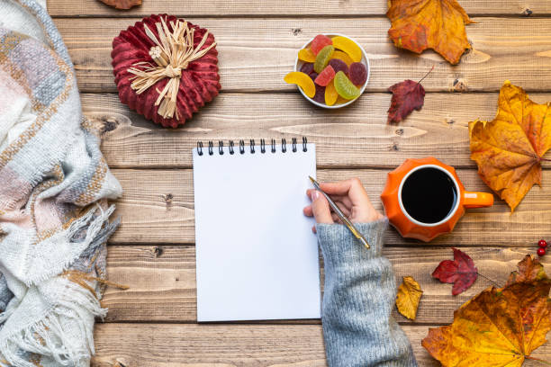 istock Desktop mock up planner. Top view composition with woman's hands in sweater, pumpkin styled cup of coffee and autumn themed decoration, fallen leaves on wooden background. Flat lay, copy space. 1279696994