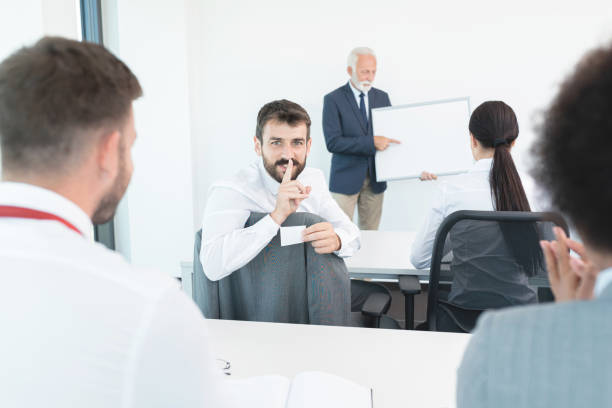 mężczyzna student oszukuje podczas wykładu w klasie - finger on lips black and white secrecy men zdjęcia i obrazy z banku zdjęć