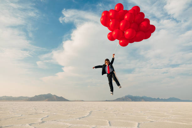 Young Business Boy with Balloons A young boy dressed in business suit, flight cap, and flying goggles holds dozens of red balloons flies his business into the profits atmosphere. Image taken at the Bonneville Salt Flats in Utah, USA. piloting photos stock pictures, royalty-free photos & images