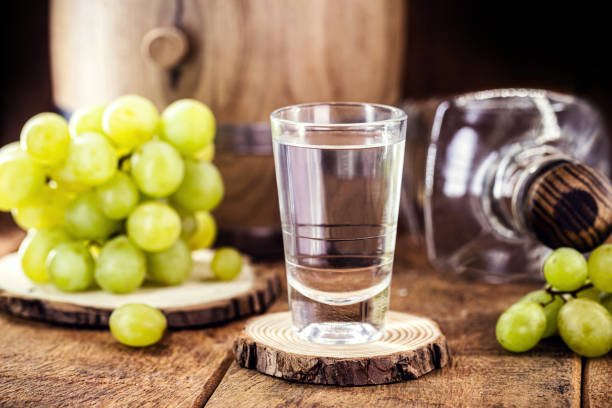 bicchiere di bevanda distillata a base di uve fermentate ad alto contenuto alcolico, su sfondo rustico in legno - vodka hard liquor bottle palinka foto e immagini stock