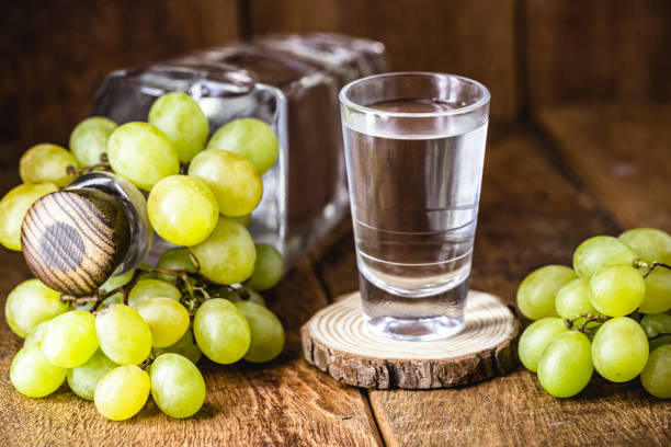 bicchiere di bevanda distillata a base di uve fermentate ad alto contenuto alcolico, su sfondo rustico in legno - vodka hard liquor bottle palinka foto e immagini stock