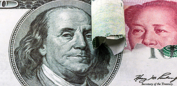 100 dollar bill tearing and revealing a hundred Chinese yuan bill in the background. Concept of dispute or crisis between the economies of China and the United States